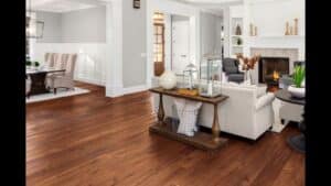 Spacious living room with hardwood floors—perfect if you’re looking to replace carpet with hardwood. Features a beige sofa, decorative console table, fireplace, and adjacent dining area with upholstered chairs.