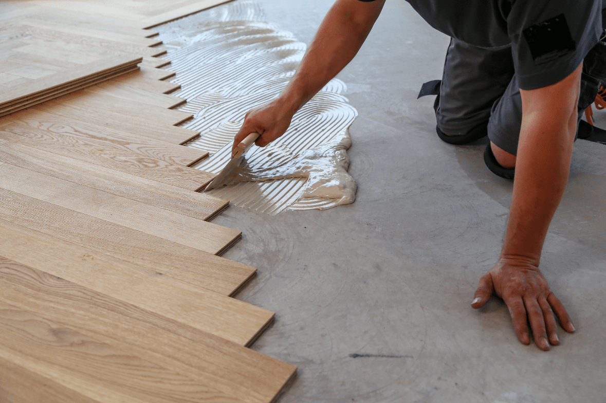 A person kneels on the floor in Utah, spreading adhesive and installing wooden panels in a staggered pattern—a step in expert commercial flooring installation.