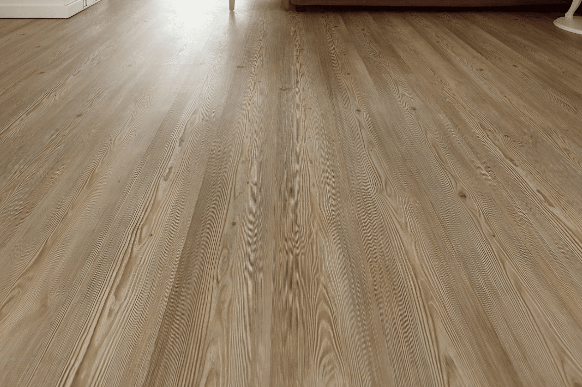 Light brown wood-grain flooring in a brightly lit room, extending toward a couch and walls in the background—an ideal showcase of Utah Flooring’s expert flooring service.