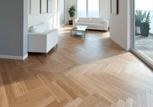 Modern living room with herringbone hardwood floor refinishing, white sofas, a glass coffee table, potted plants, and floor-to-ceiling windows leading to a balcony.