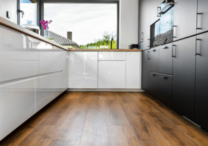 Modern kitchen with glossy white and matte black cabinets, hardwood floor refinishing, large window, and a countertop holding a plant and appliances. A comprehensive guide to elegant design meets practical function.